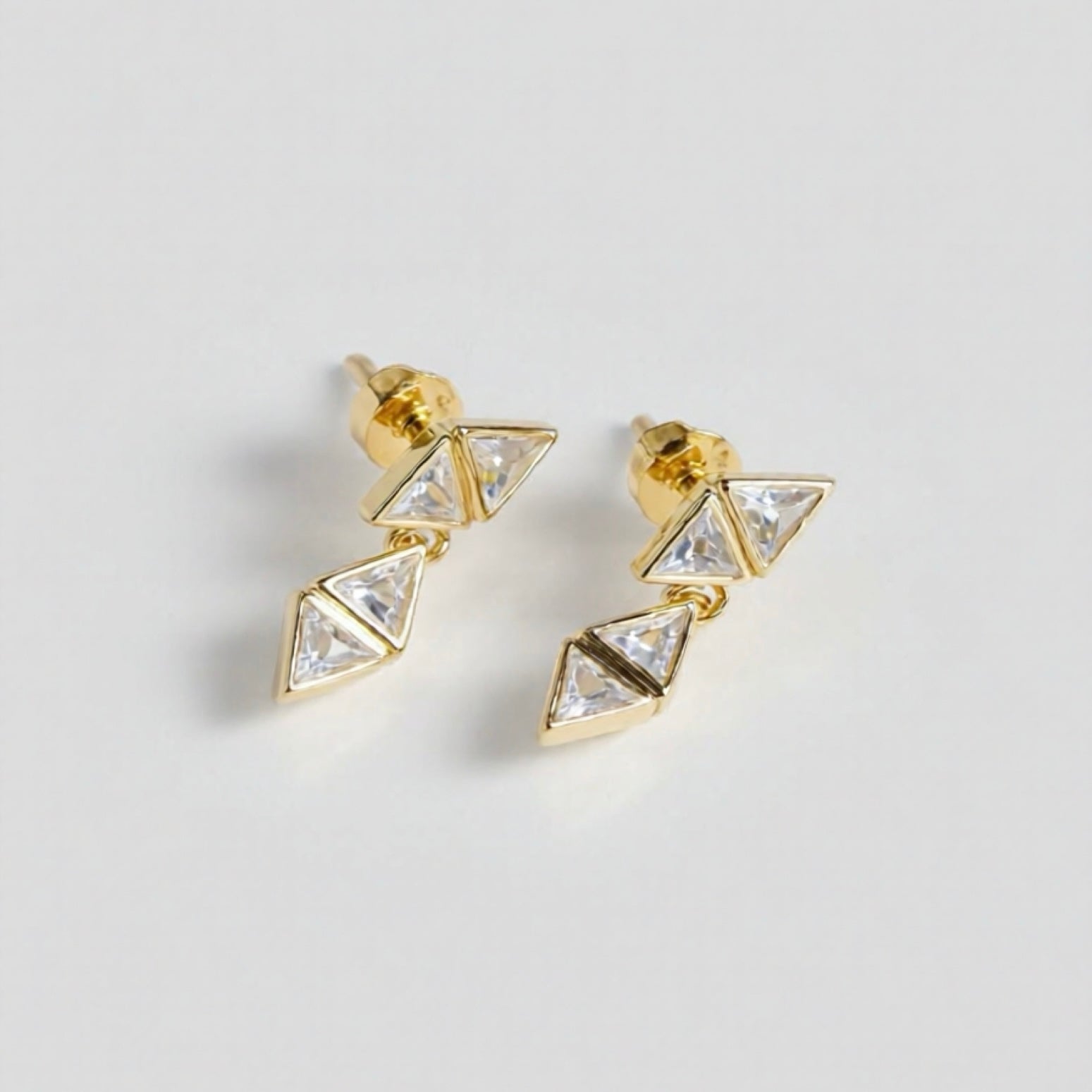 Gold triangle-shaped earrings with clear stones on a light gray background