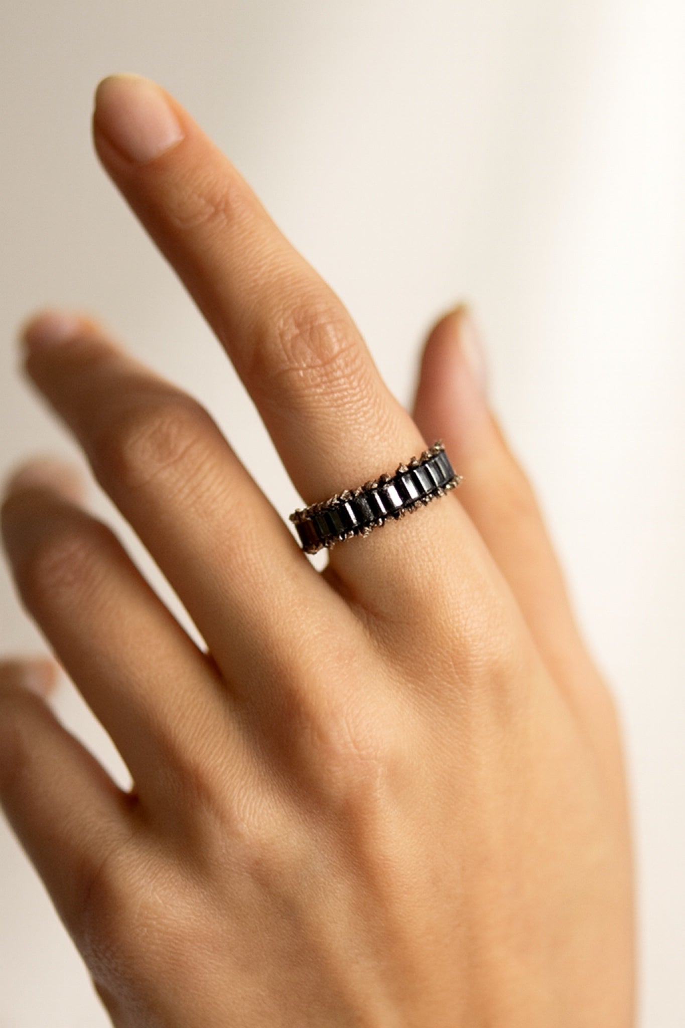 Hand wearing a black beaded ring on a neutral background