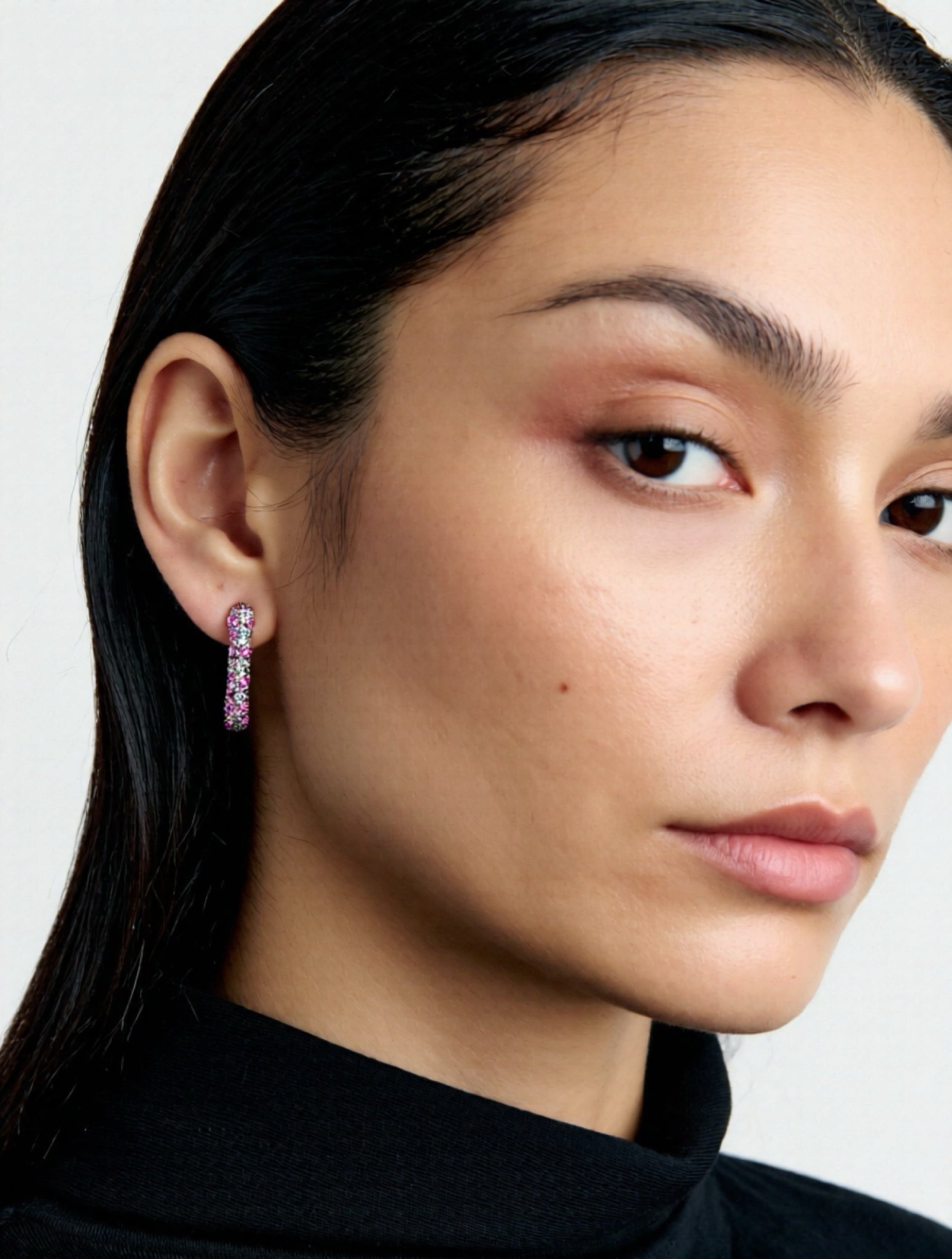 Close-up of a woman wearing pink hoop earrings with a plain background