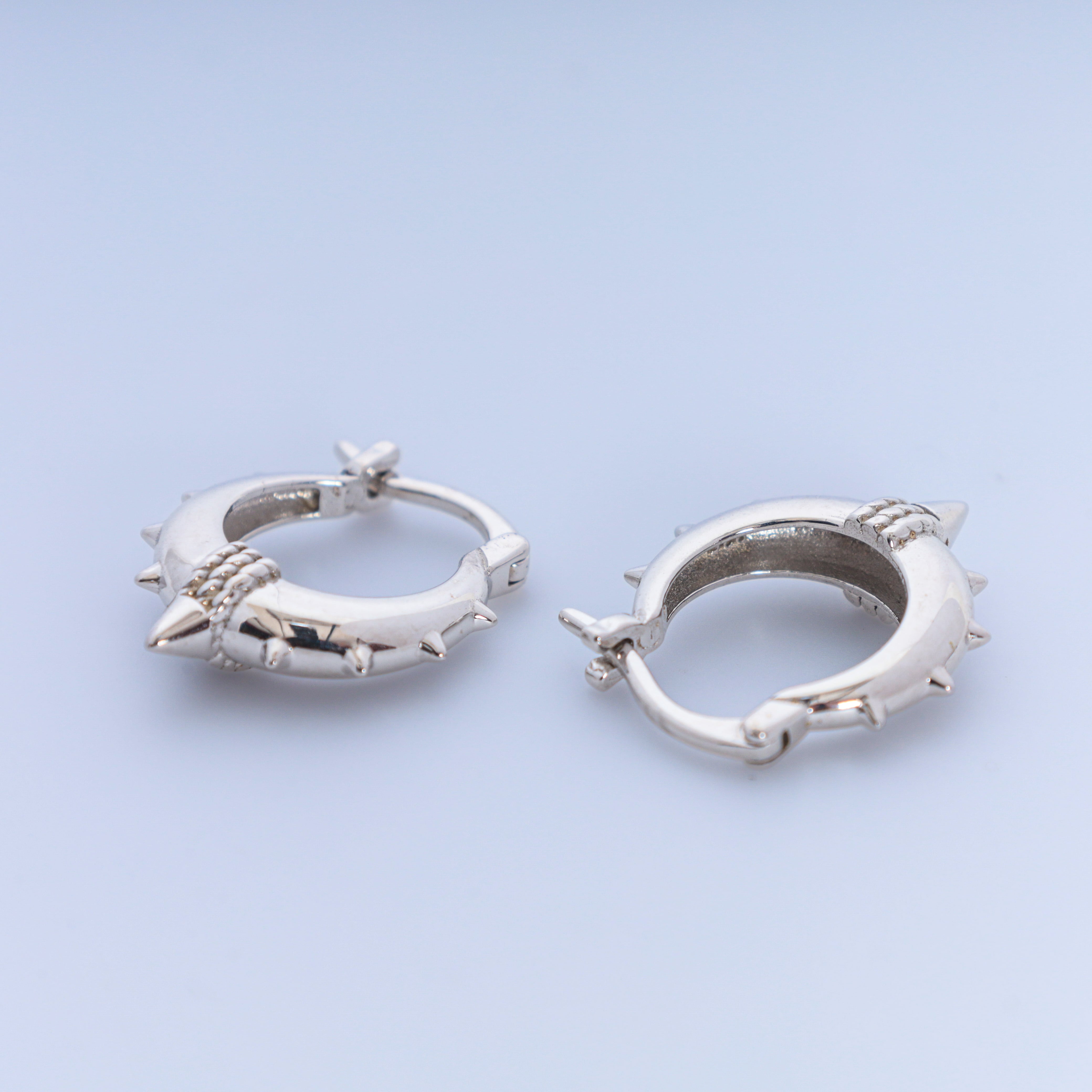 Silver hoop earrings with spike details on a light blue background