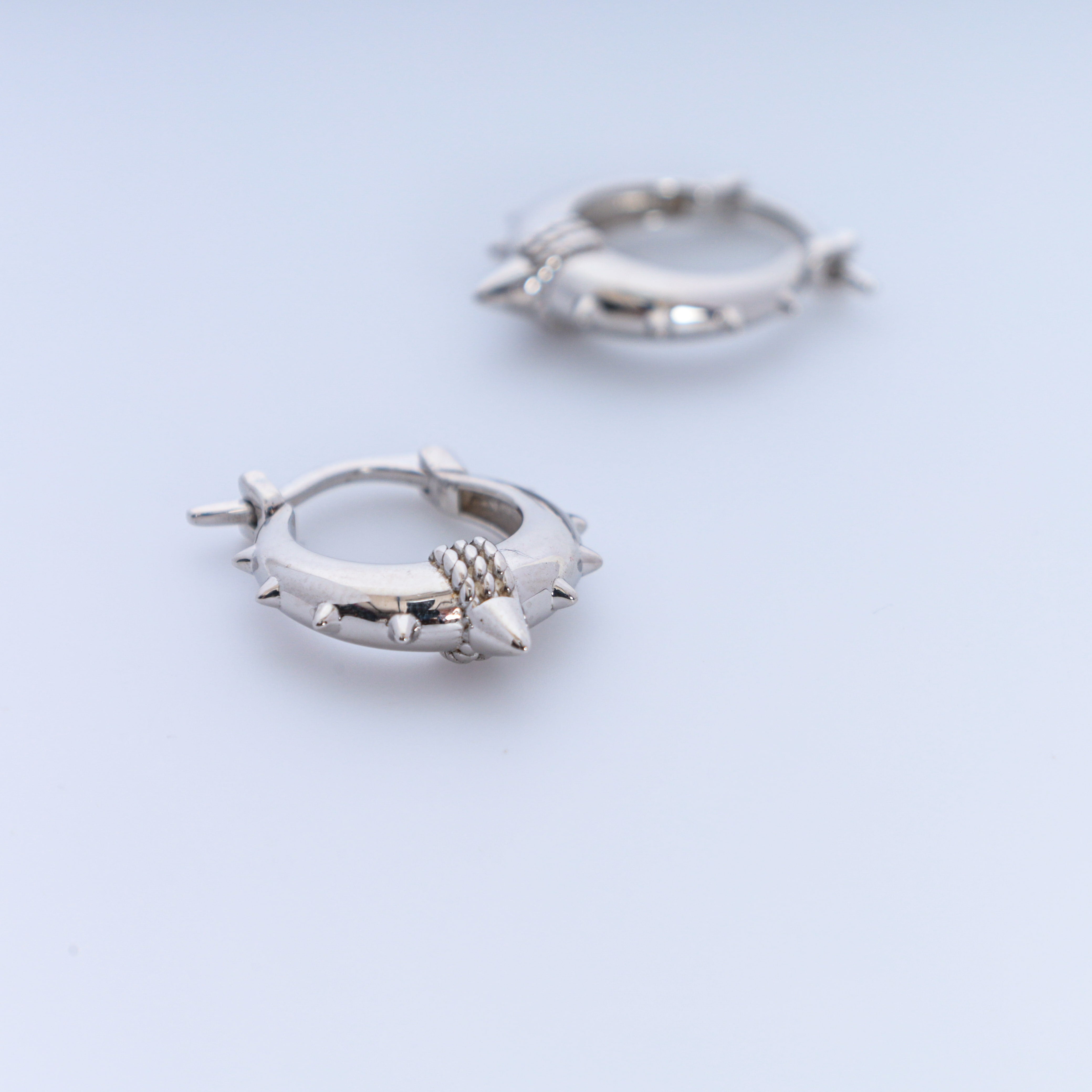 Pair of silver hoop earrings with spike details on a light blue background