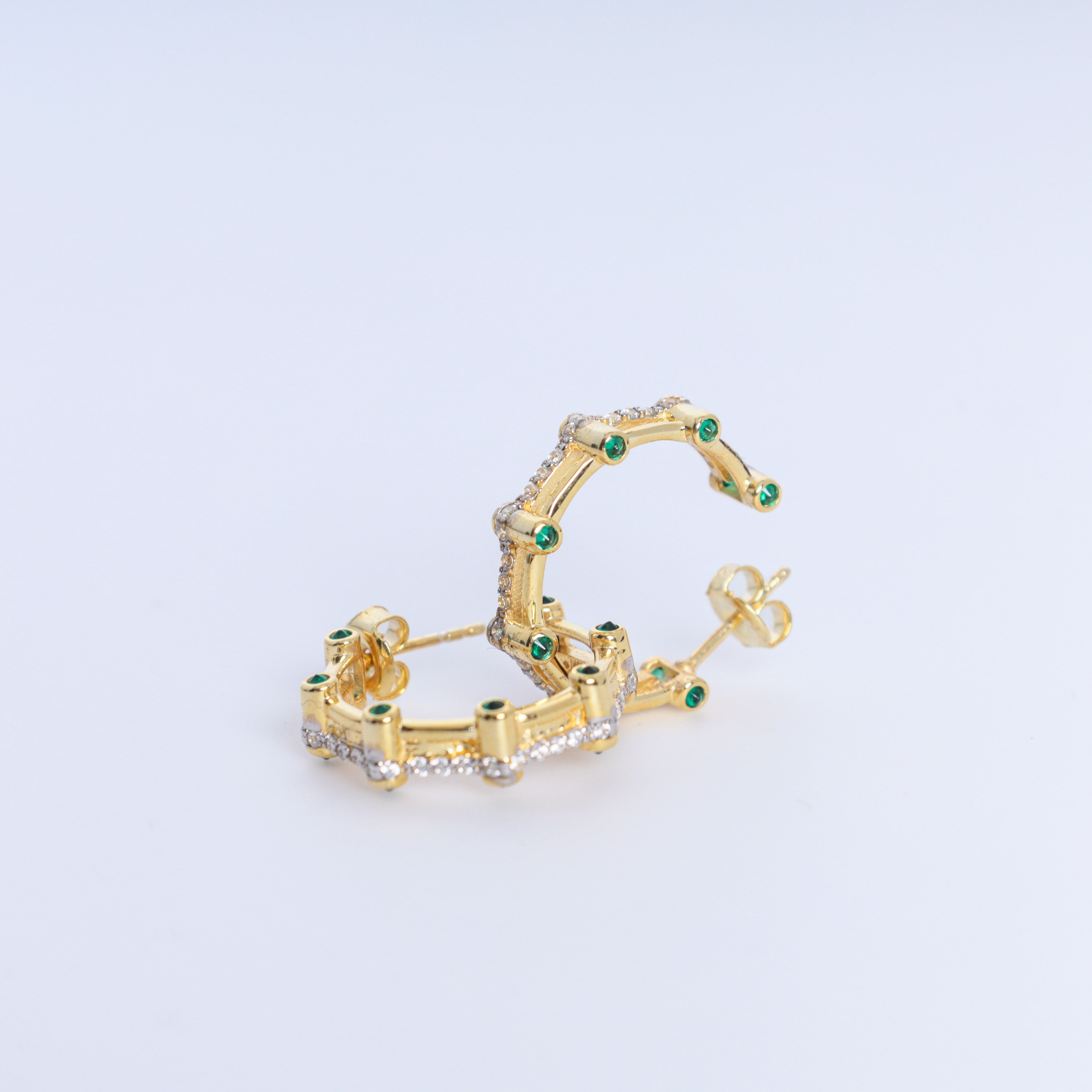 Gold hoop earrings with green gemstones on a light gray background