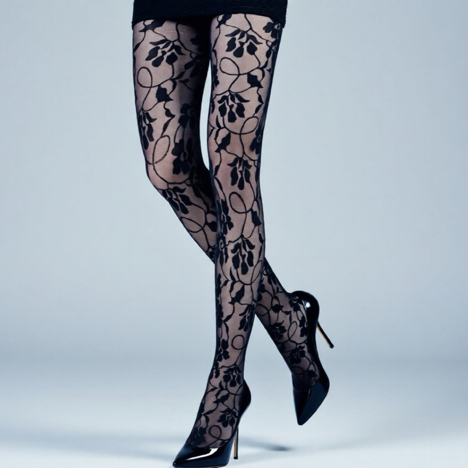 Black floral lace tights worn with black high heels on a light gray background