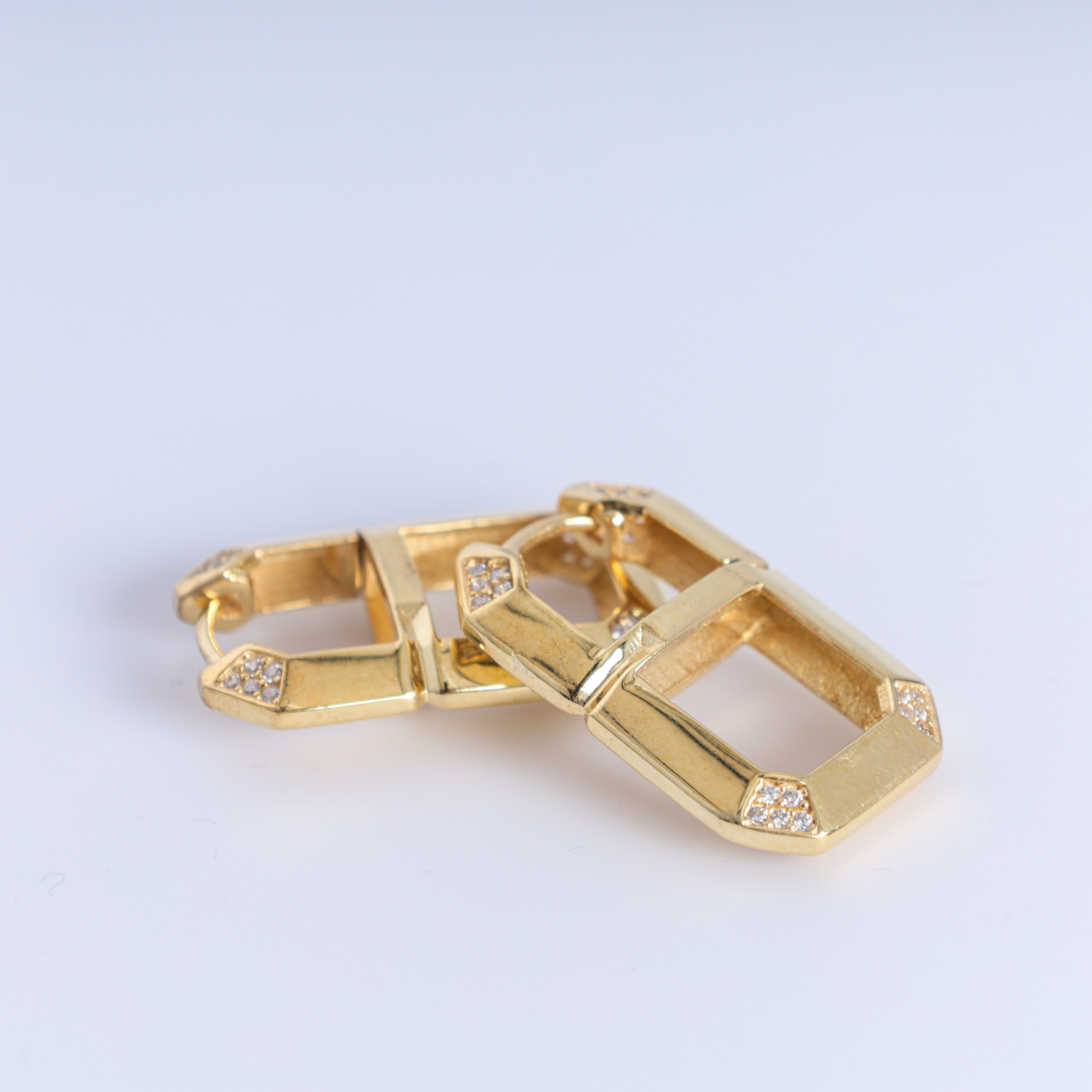 Gold earrings with diamond-like stones on a light gray background