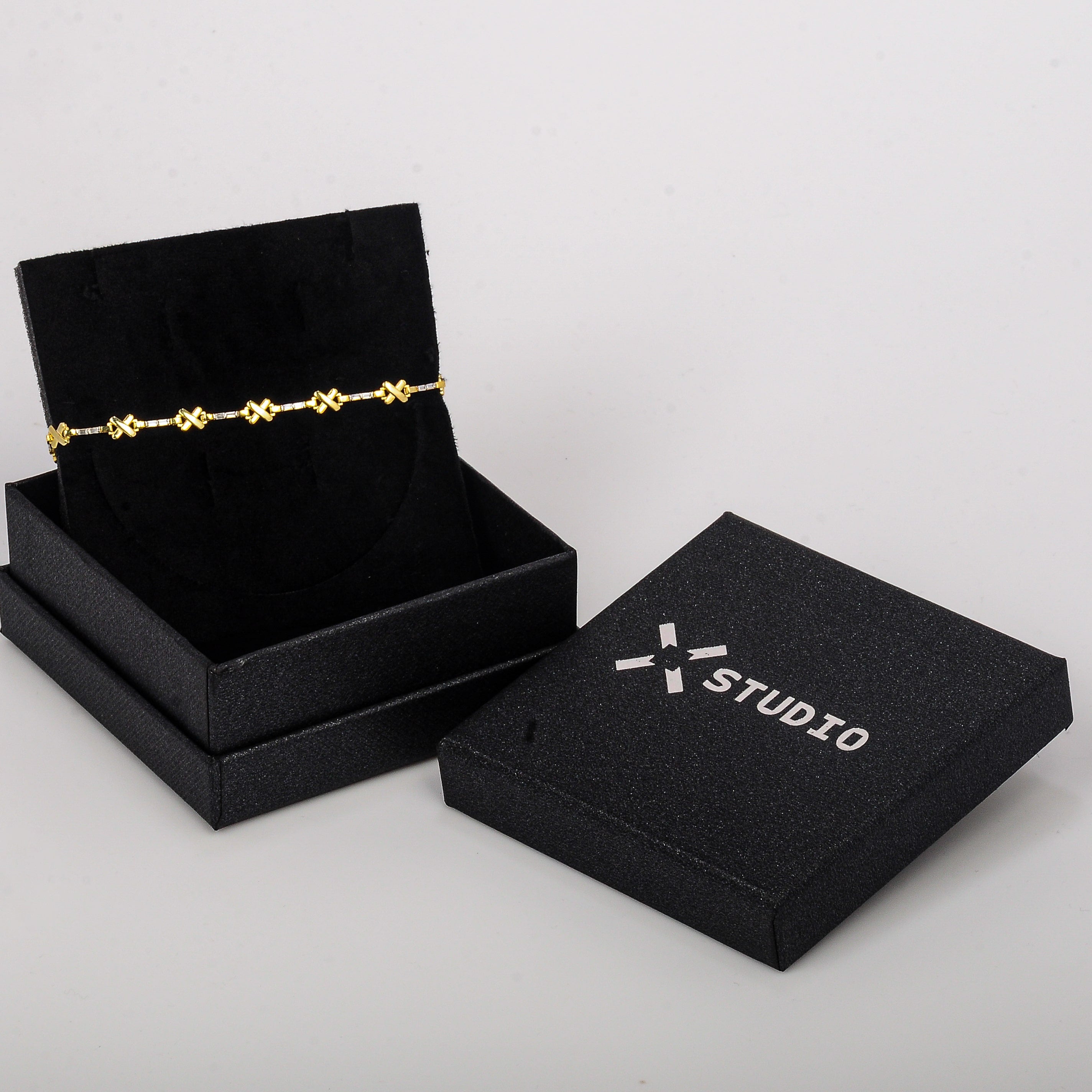 Gold bracelet in an open black jewelry box with 'X Studio' branding on a light gray background