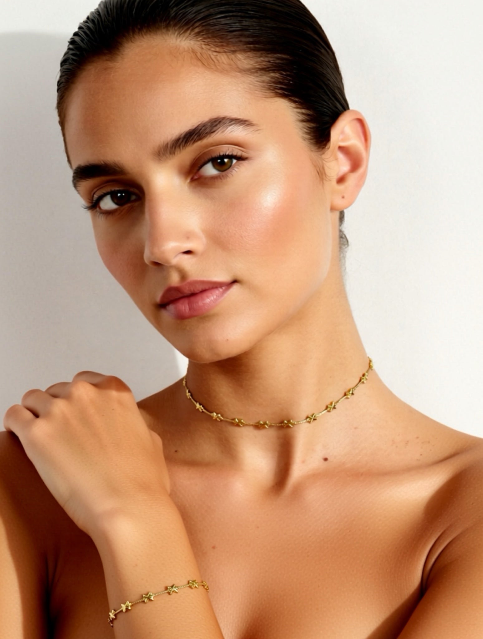 Woman wearing a gold necklace and bracelet against a neutral background