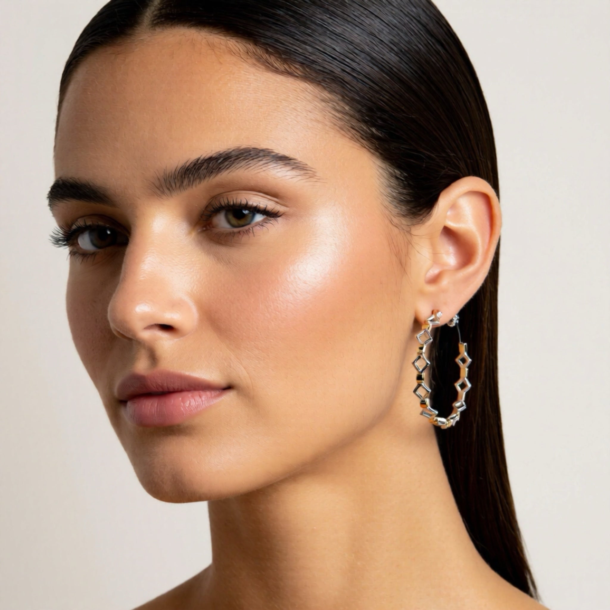 Close-up of a woman wearing silver hoop earrings with a neutral background