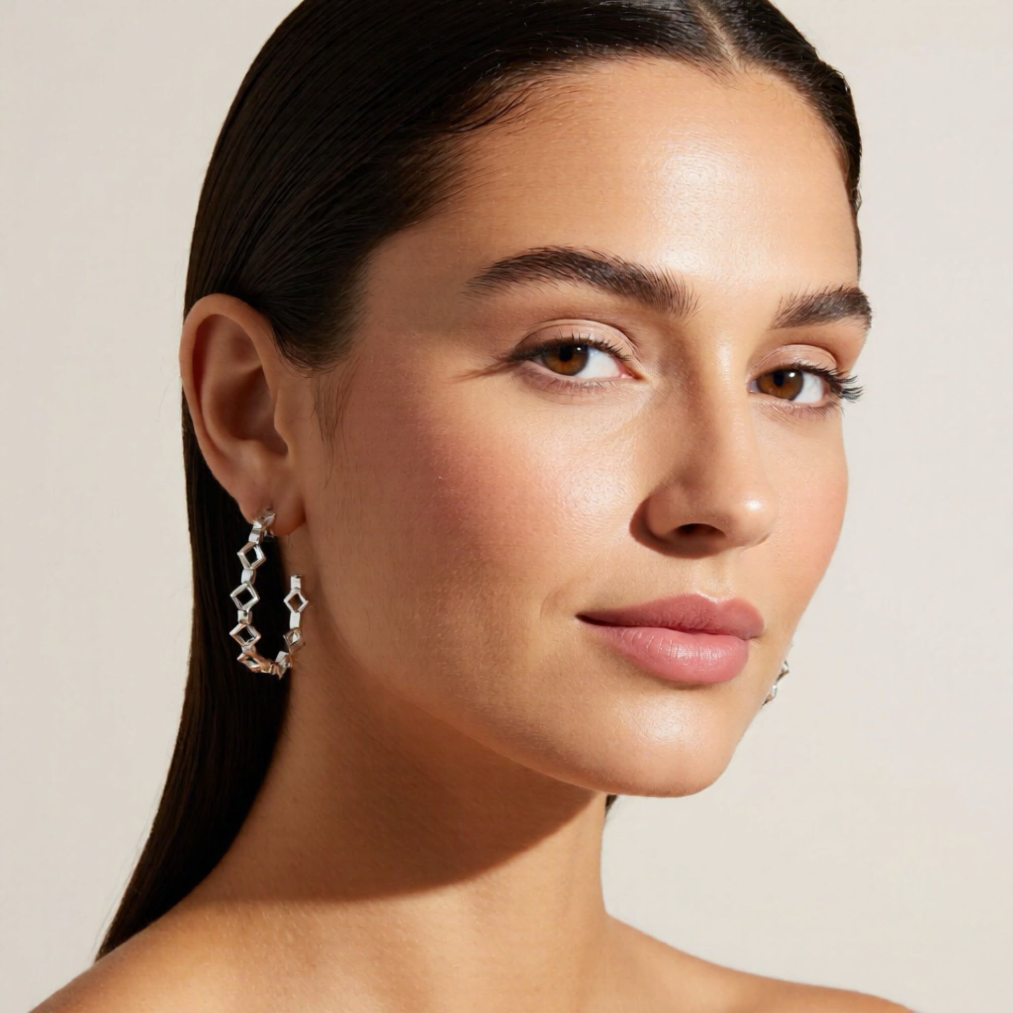 Close-up of a woman wearing a silver earring against a beige background