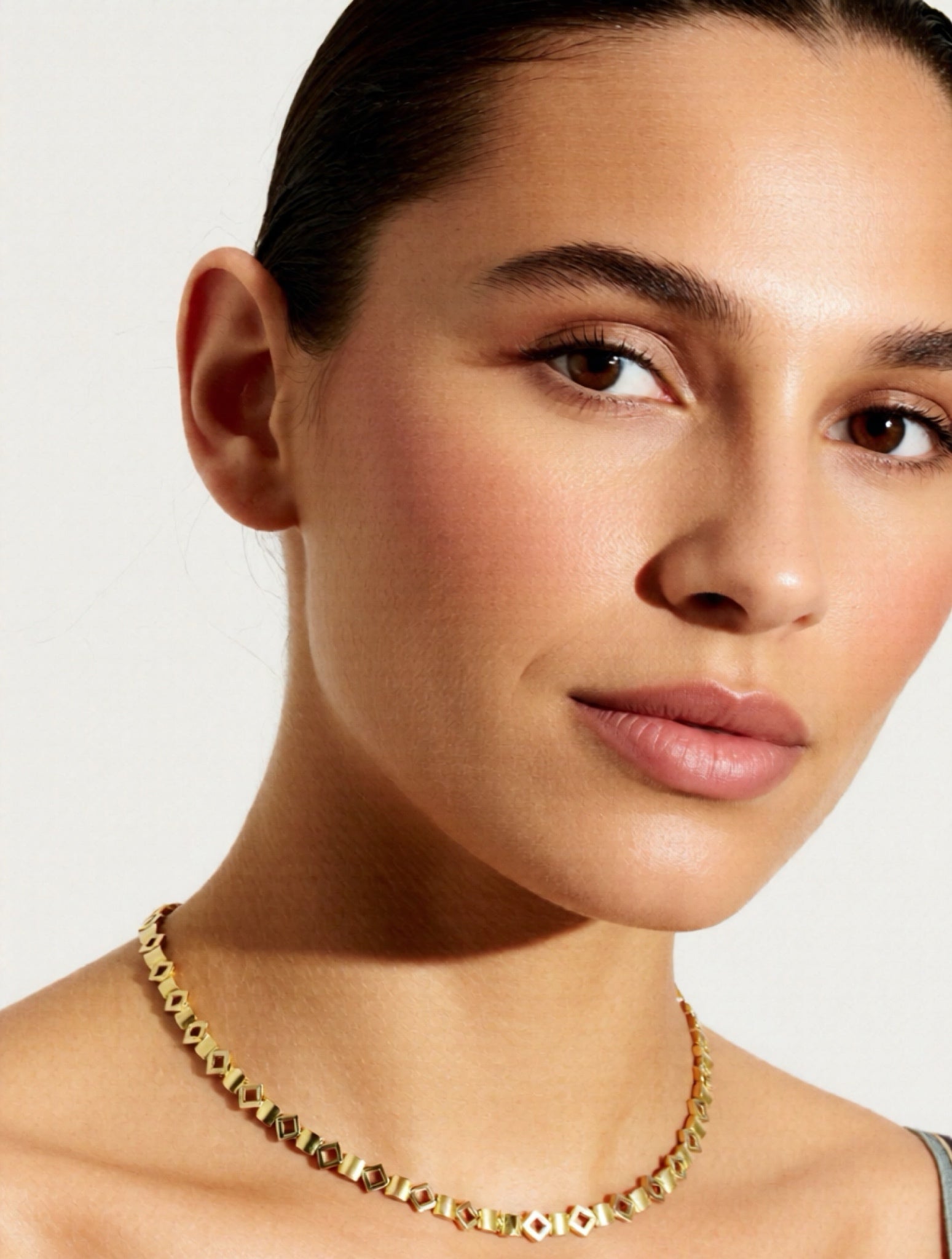 Close-up of a person wearing a gold necklace against a neutral background