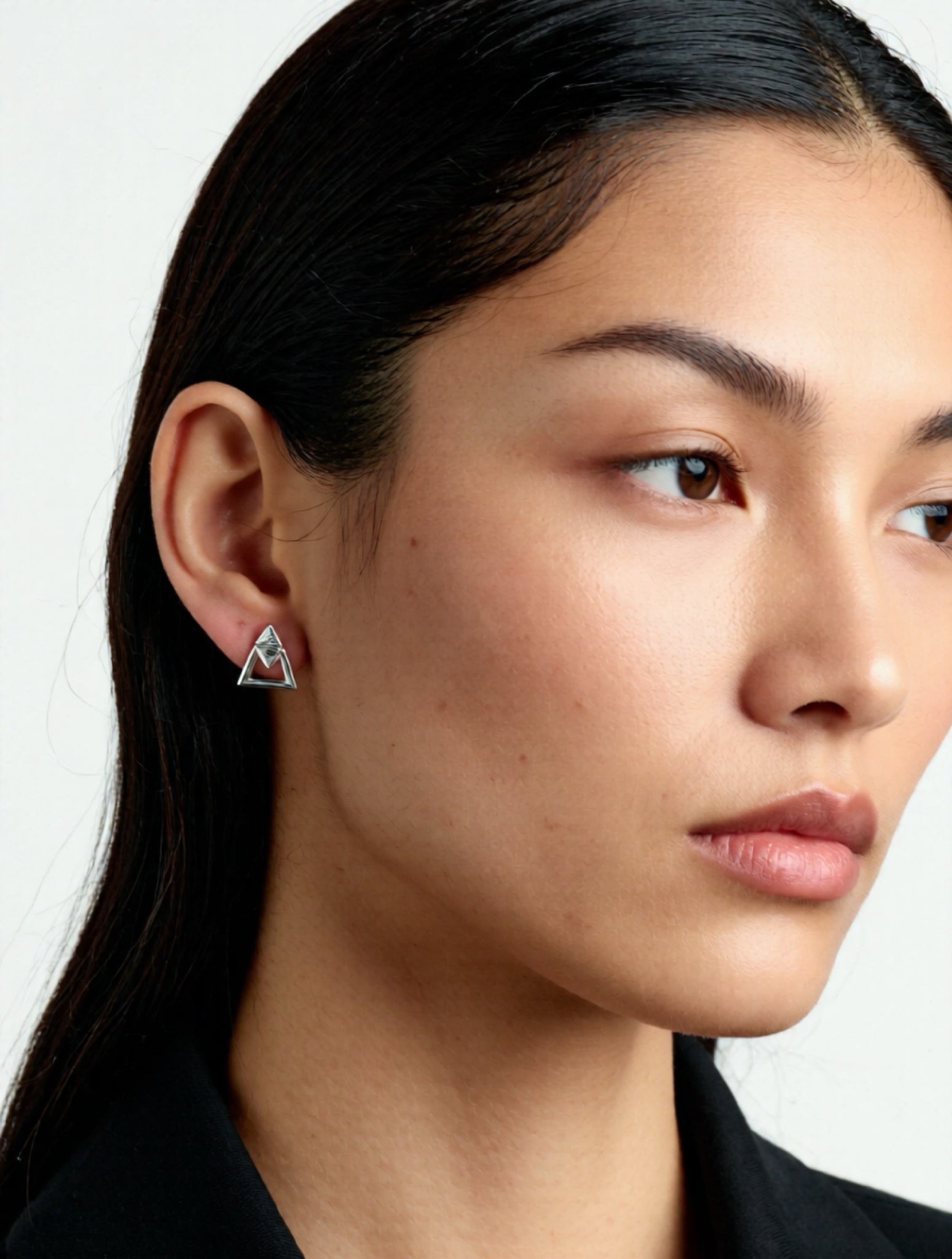 Close-up of a person wearing a triangular earring against a plain background
