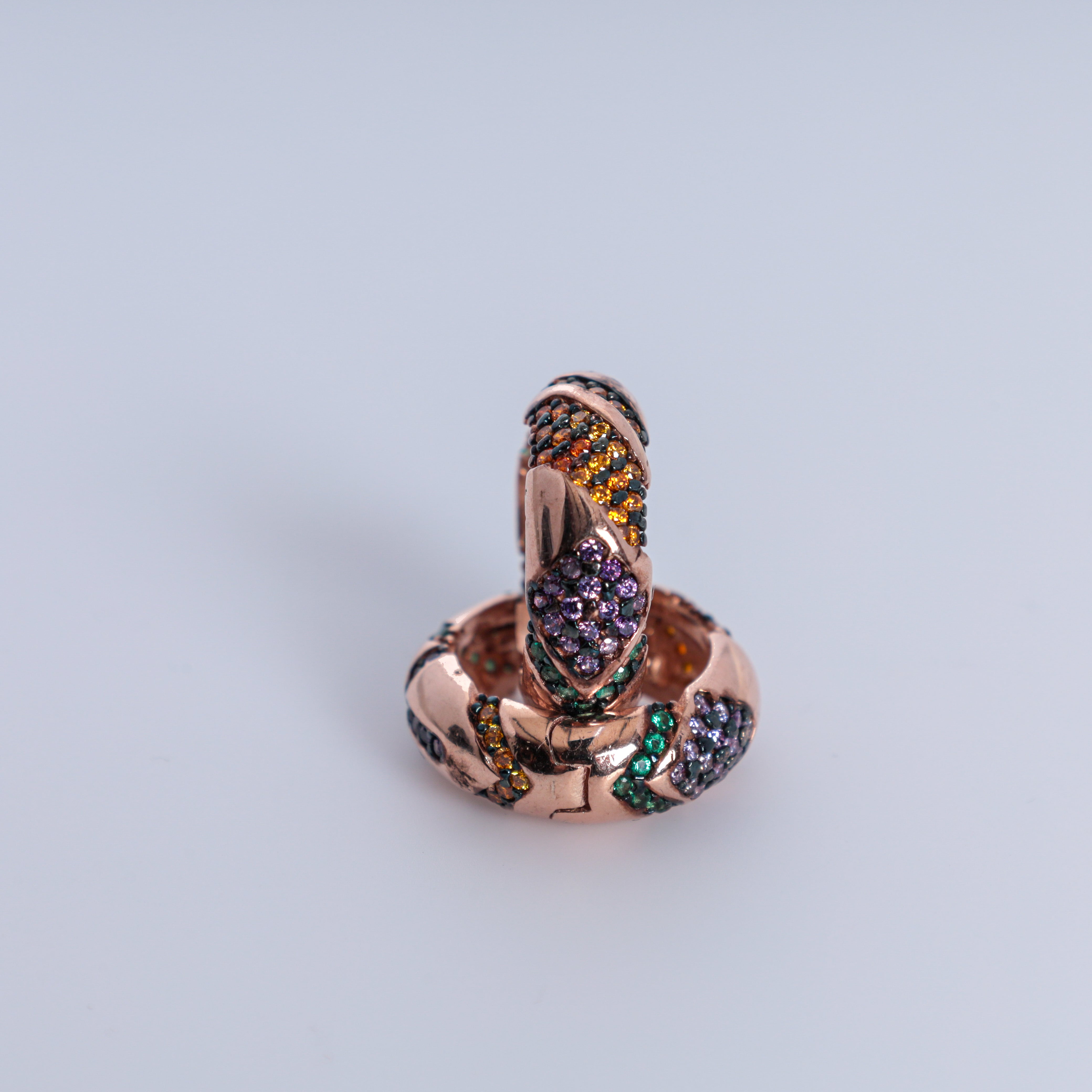 Jewelry charm shaped like a snake with multicolored stones on a light gray background