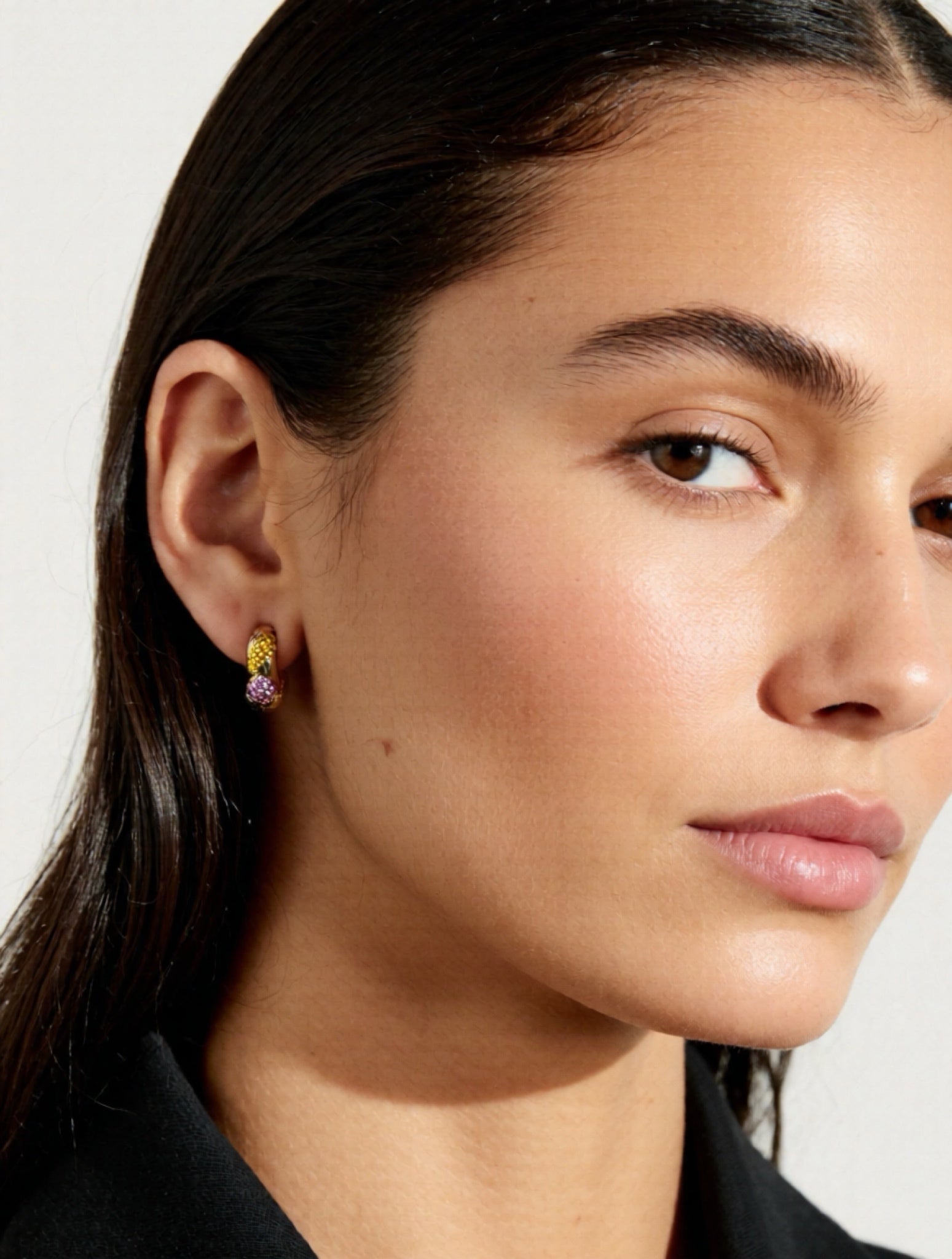 Close-up of a woman wearing colorful earrings with a neutral background