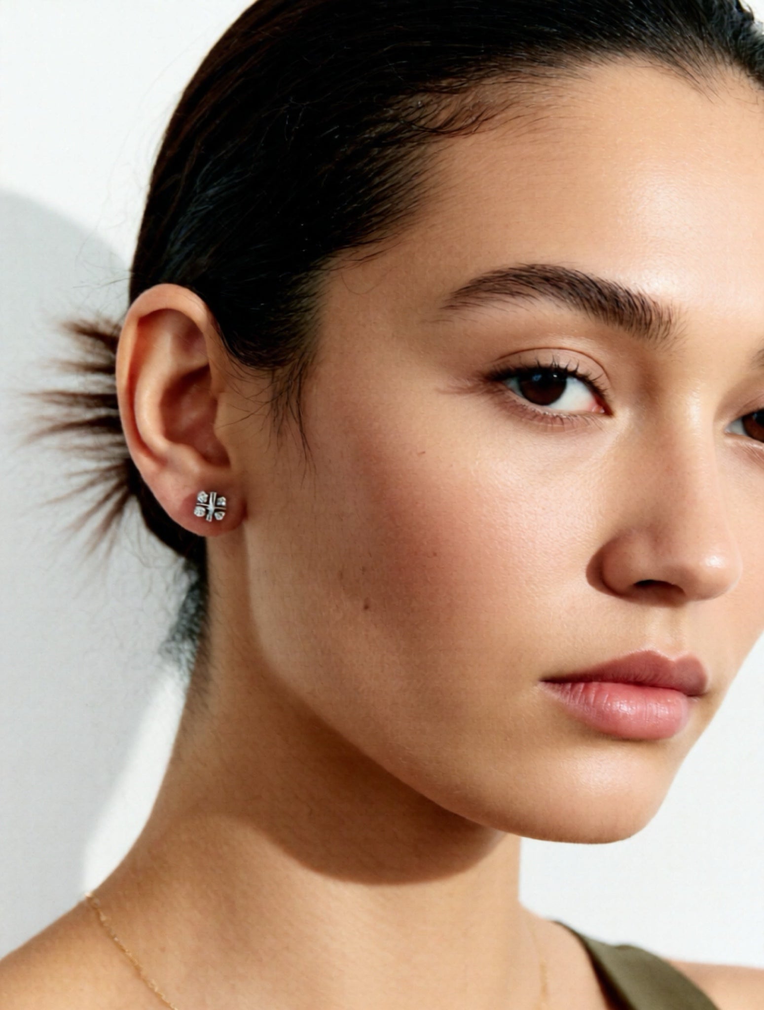 Close-up of a woman's ear with a diamond earring against a neutral background
