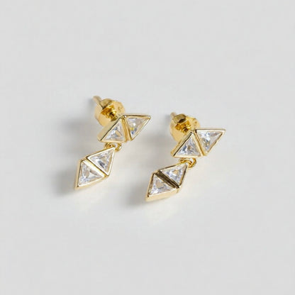Gold triangle-shaped earrings with clear stones on a light gray background