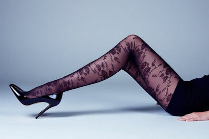Legs wearing black floral lace tights on a light gray background