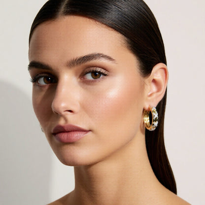 Close-up of a woman wearing gold hoop earrings with a neutral background