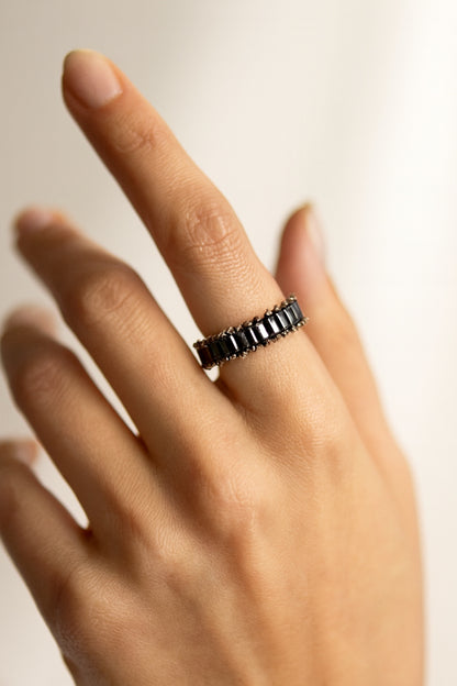 Hand wearing a black beaded ring on a neutral background