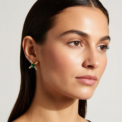 Close-up of a woman wearing a gold earring with a green gemstone on a neutral background