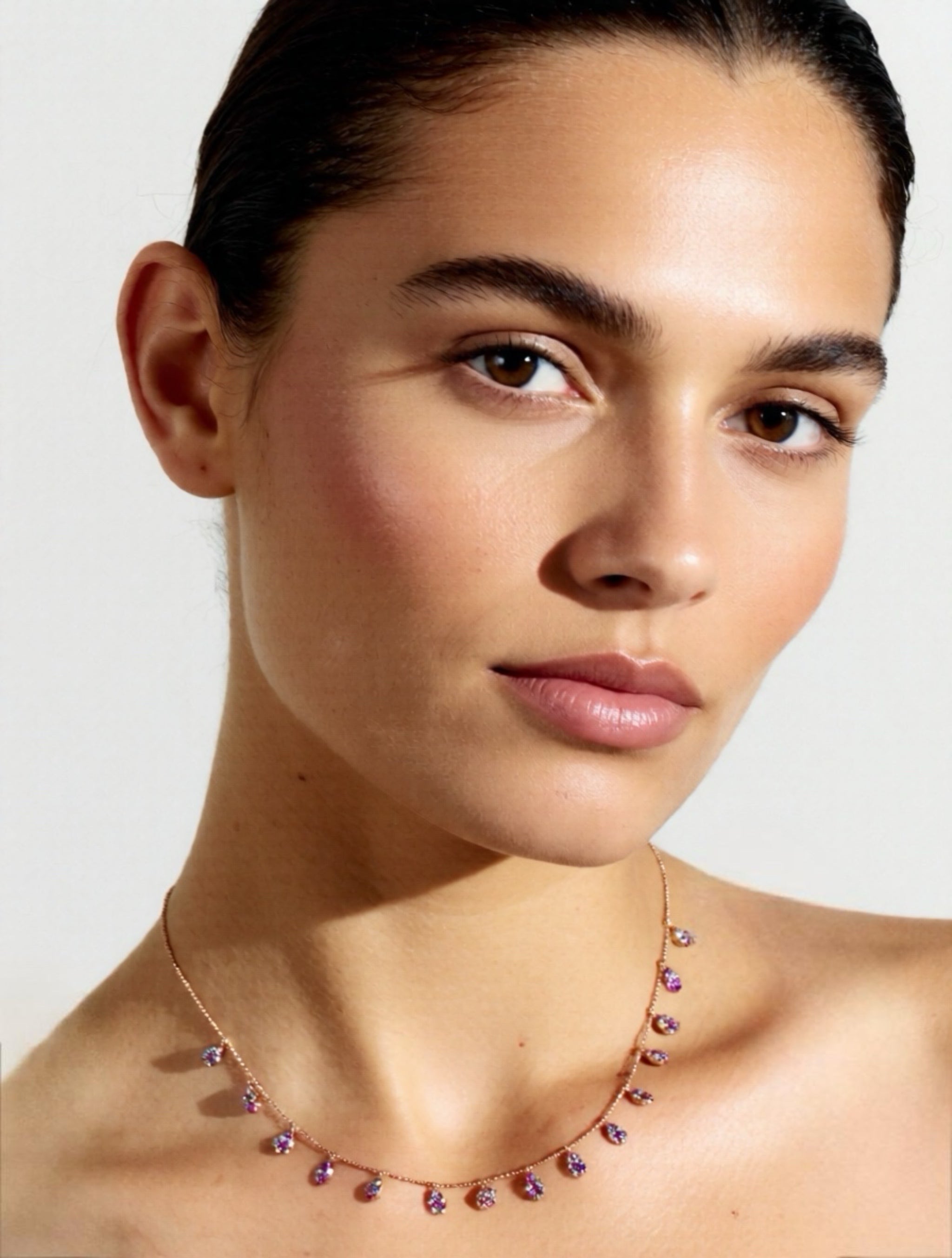 Woman wearing a delicate necklace with a plain background