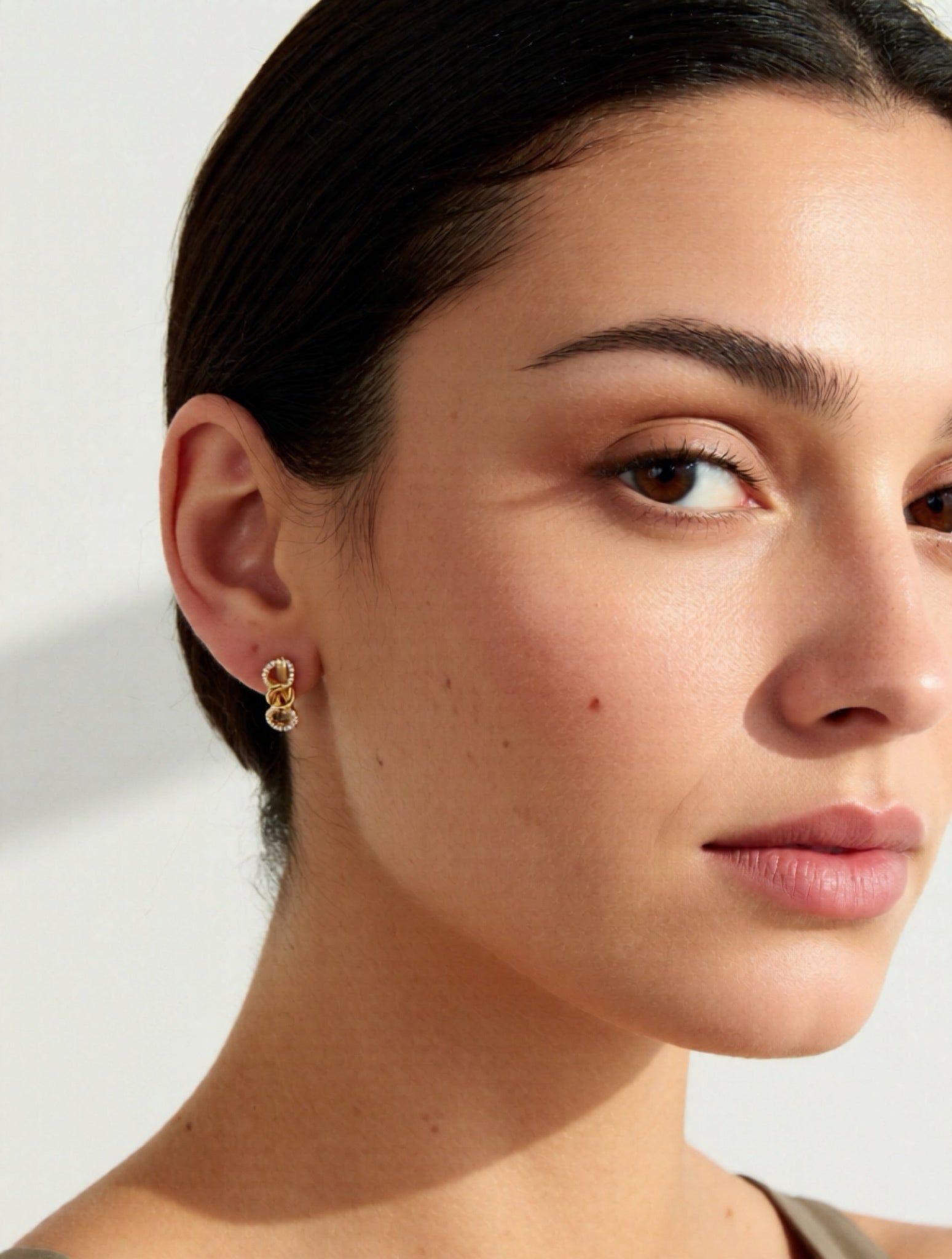 Close-up of a woman wearing gold earrings with a neutral background