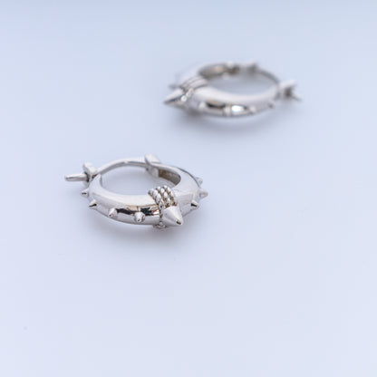Pair of silver hoop earrings with spike details on a light blue background