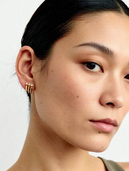 Close-up of a person wearing gold earrings with a neutral background