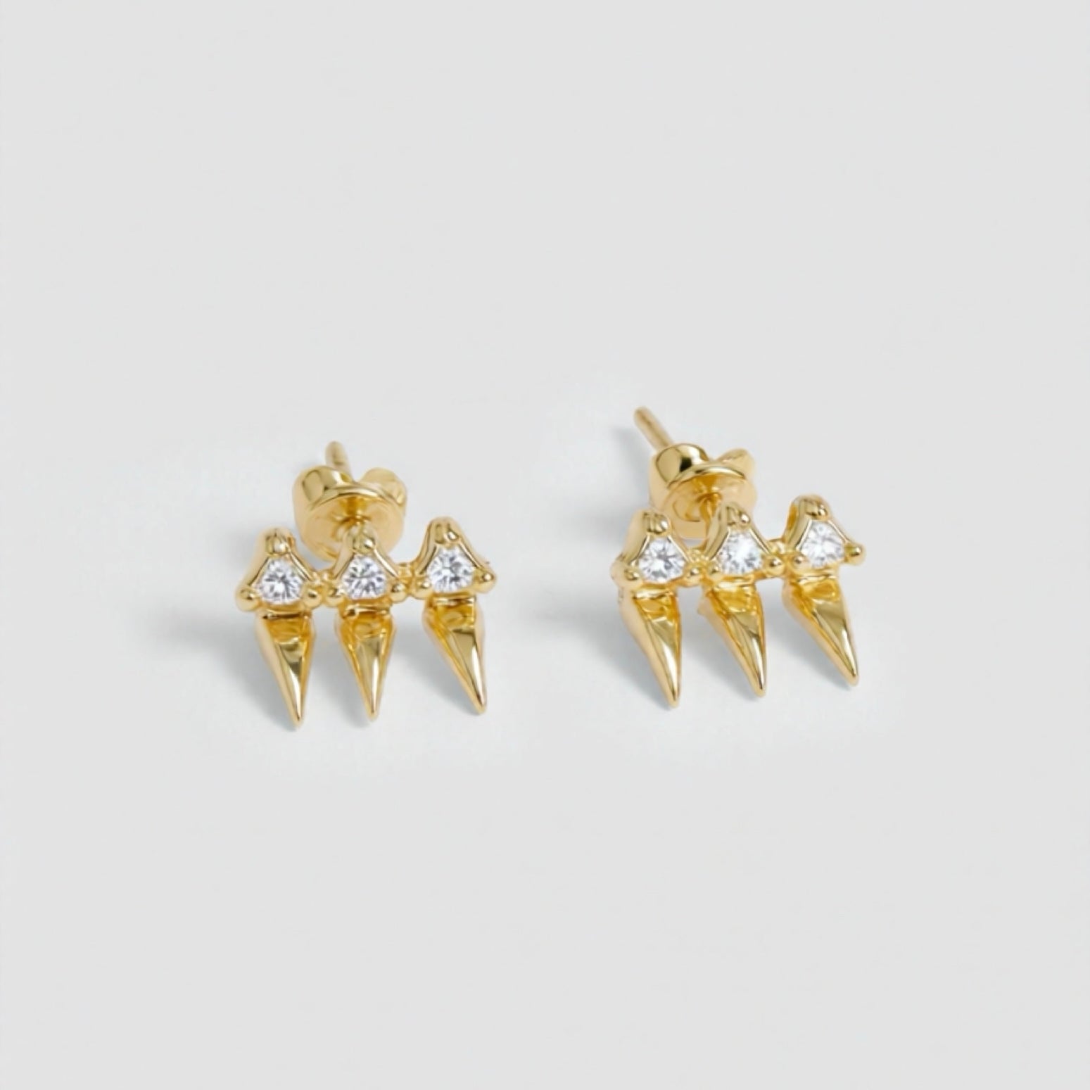 Gold spike earrings with clear gemstones on a light gray background
