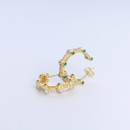 Gold hoop earrings with green gemstones on a light gray background