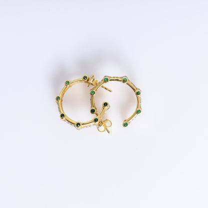 Gold hoop earrings with green gemstones on a light gray background