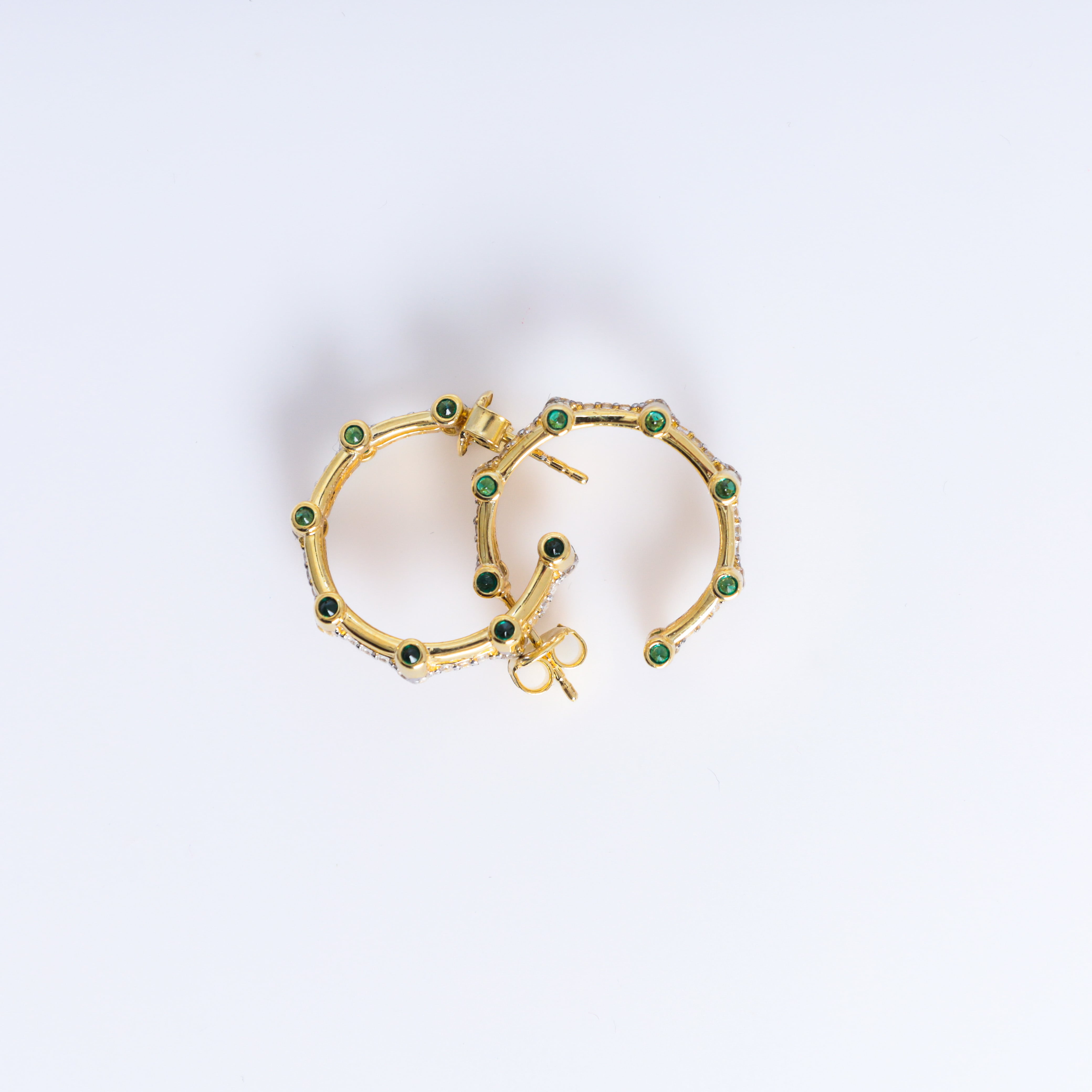 Gold hoop earrings with green gemstones on a light gray background