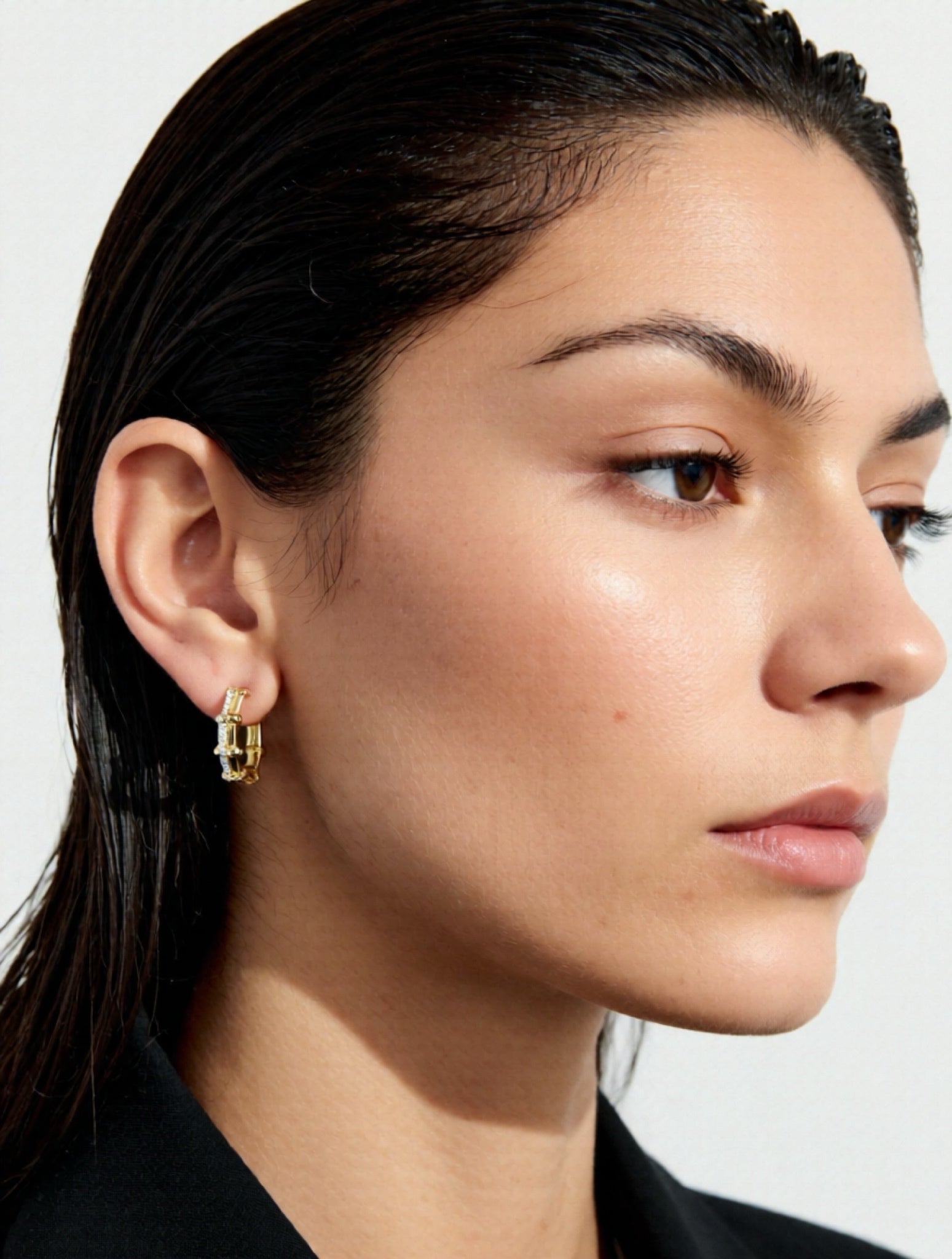 Close-up of a woman wearing gold hoop earrings with a plain background