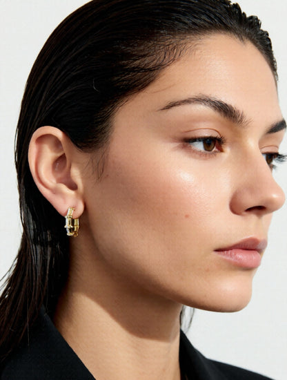 Close-up of a woman wearing gold hoop earrings with a plain background