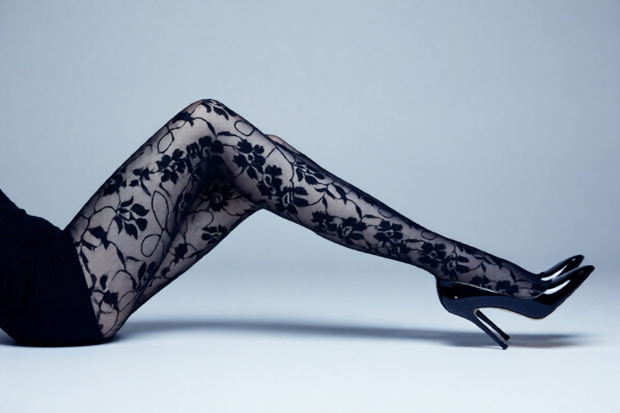 Black floral lace tights worn by a person on a light gray background