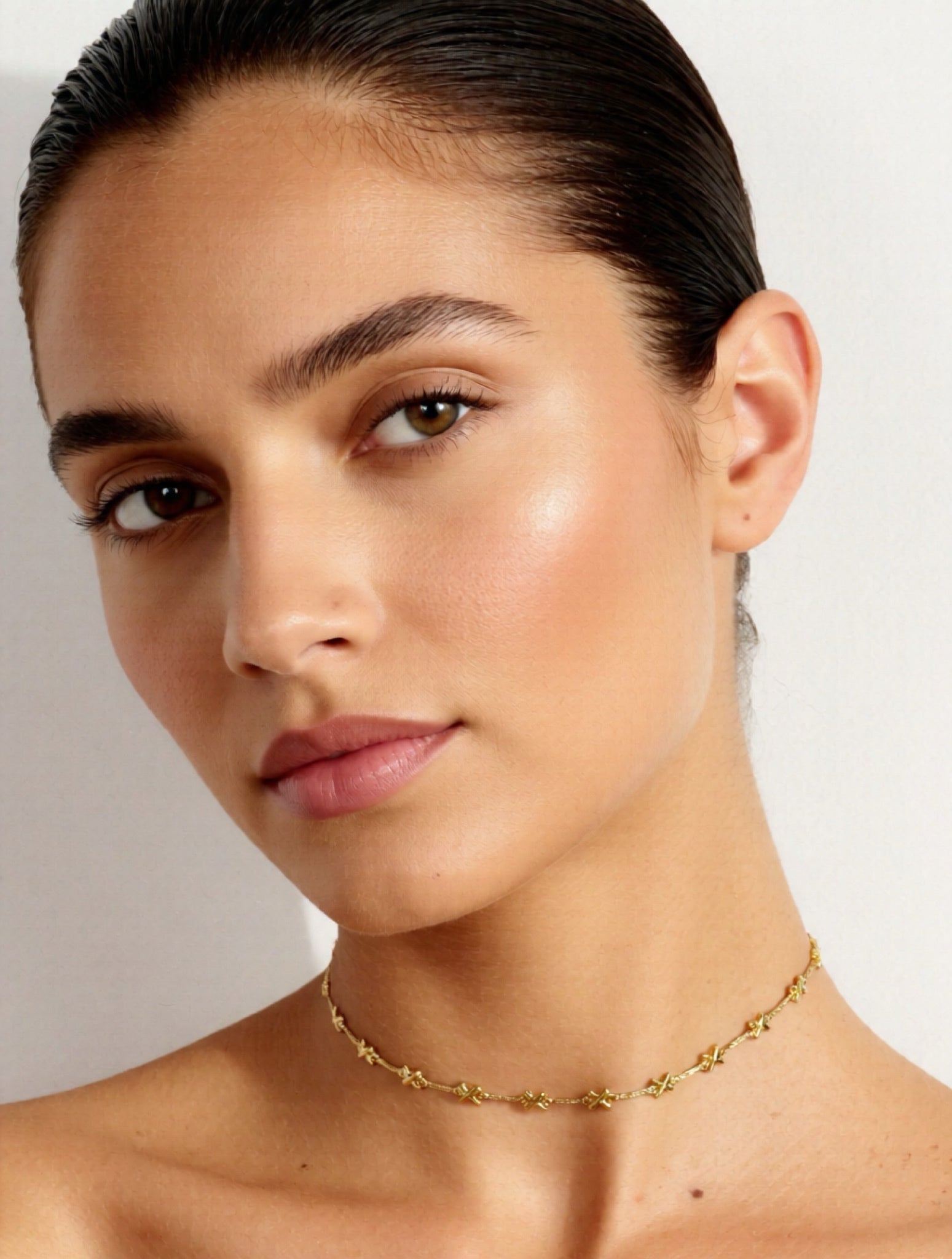 Close-up of a woman wearing a gold necklace against a neutral background