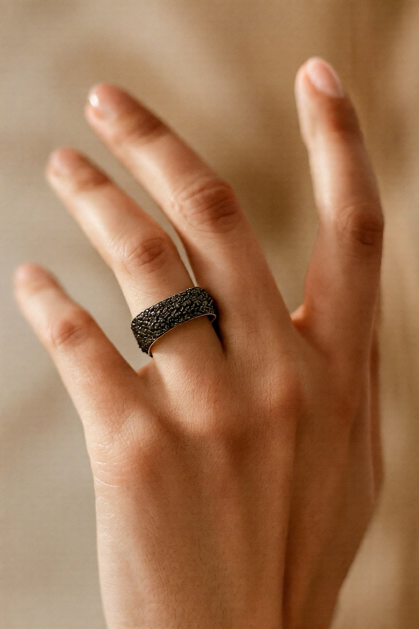Hand wearing a textured black ring on a neutral background