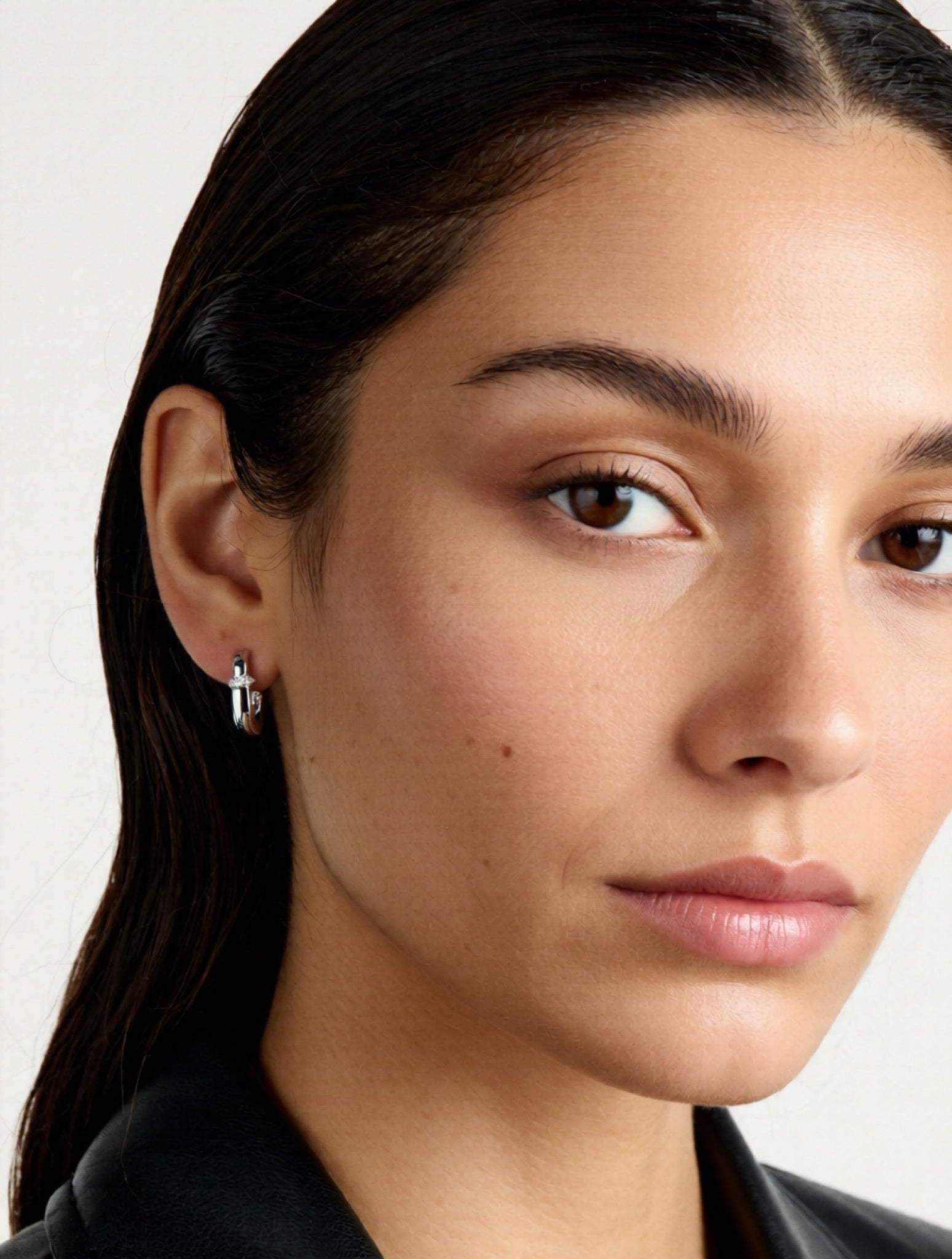 Close-up of a person wearing a silver cross earring on a plain background