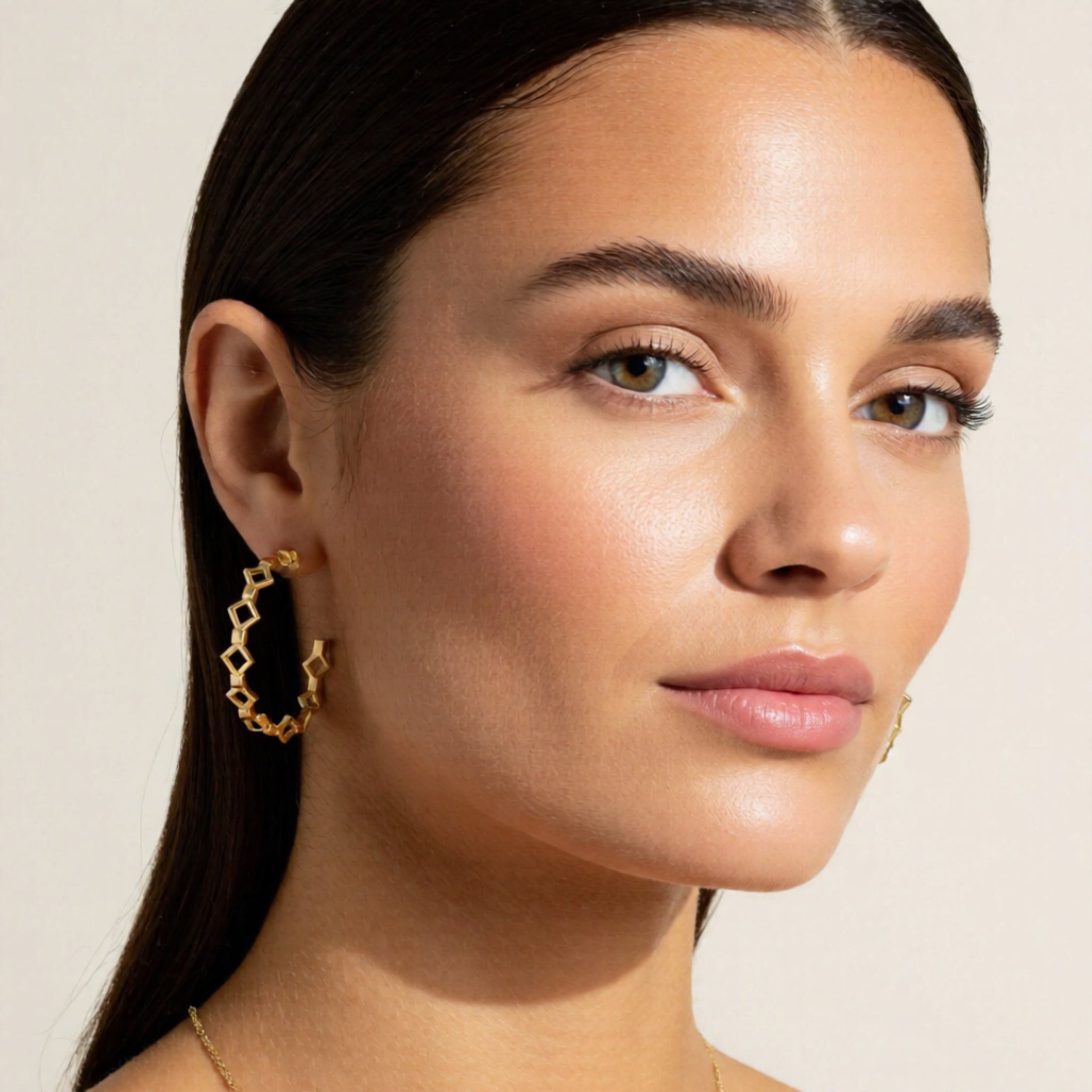 Close-up of a woman wearing gold earrings with a neutral background