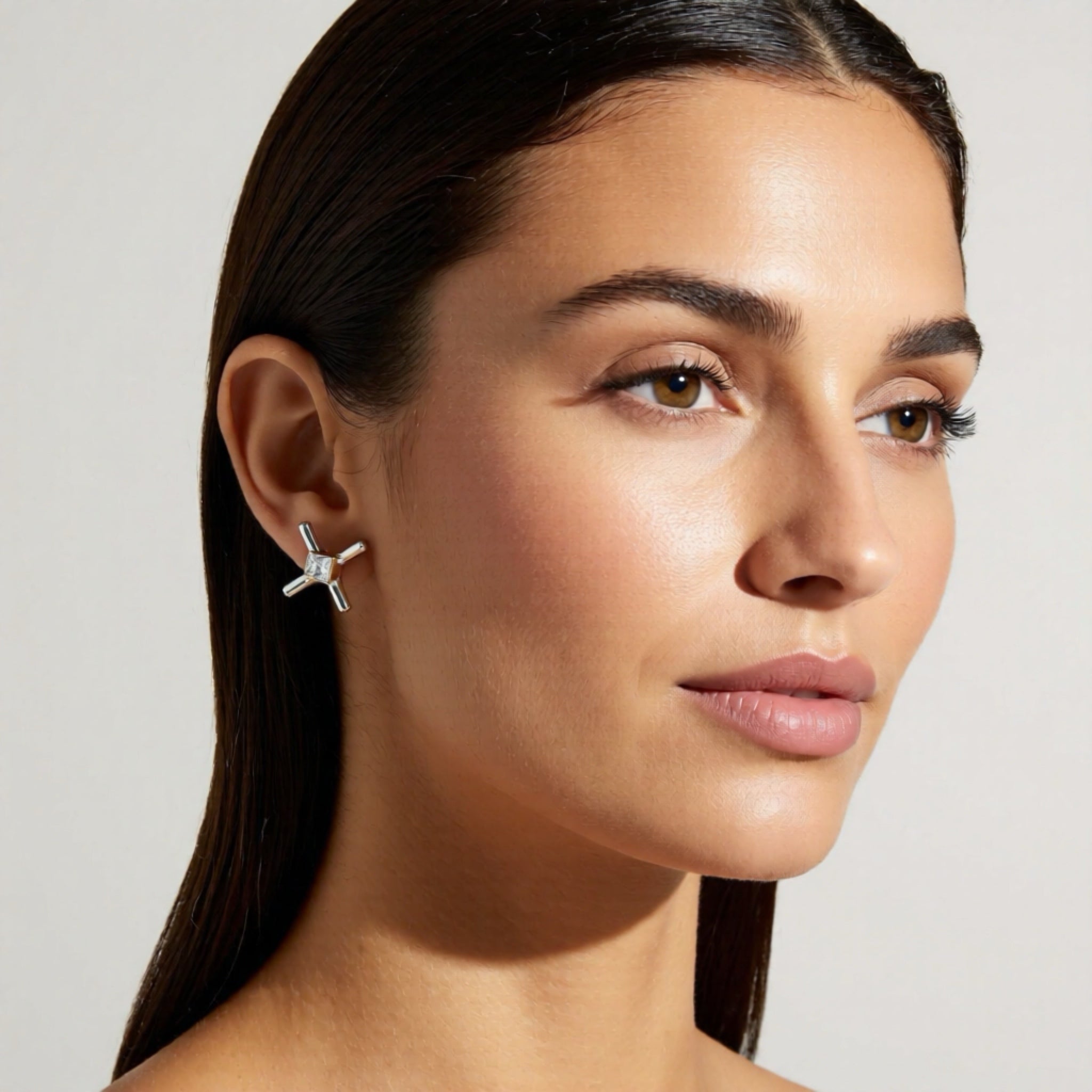 Close-up of a woman wearing a silver earring against a neutral background