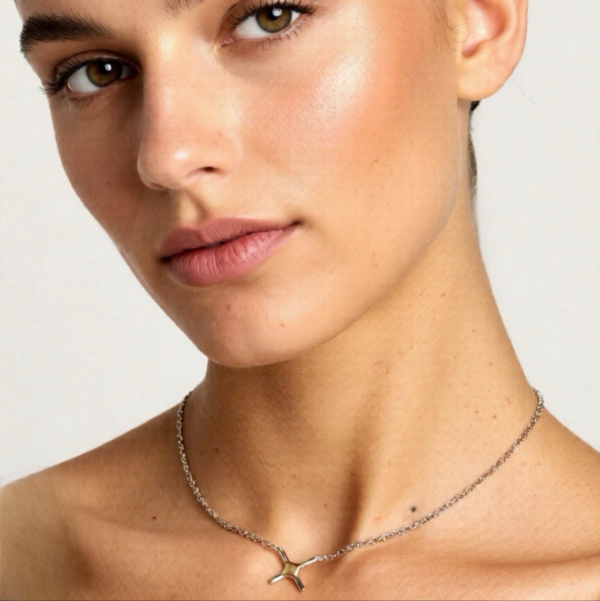 Close-up of a woman wearing a necklace with a cross pendant on a plain background