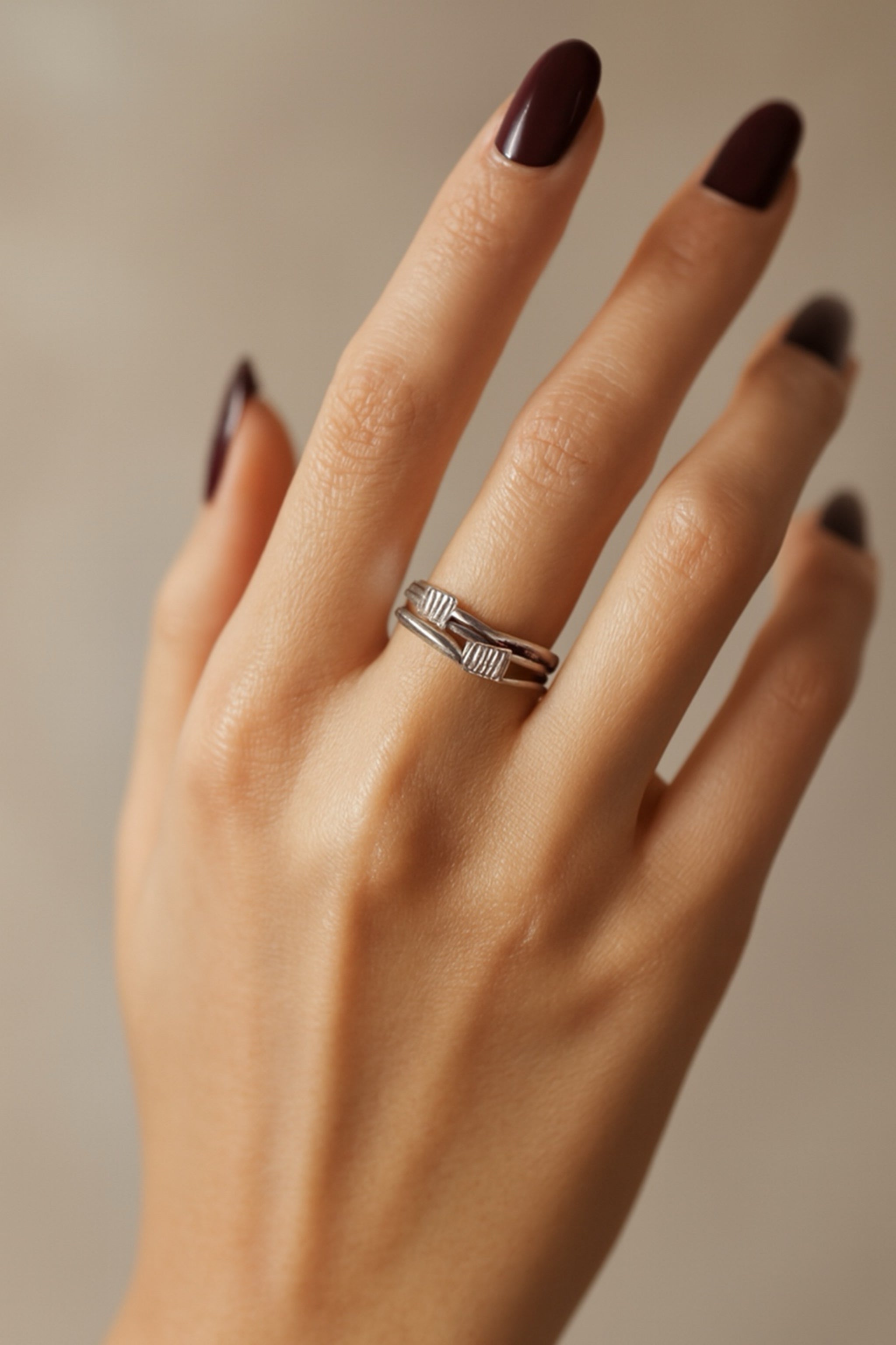 Hand wearing a silver ring with dark nail polish on a neutral background