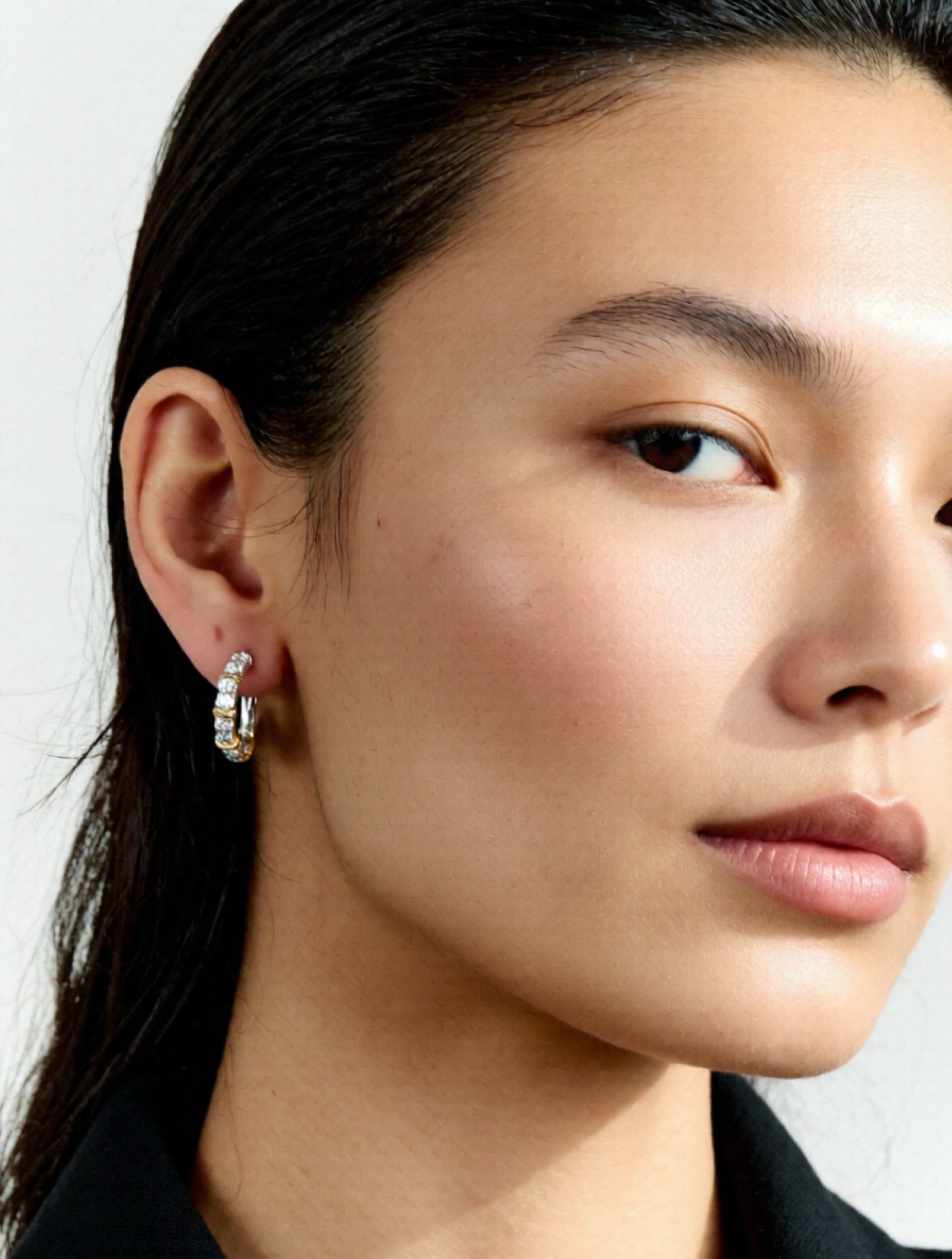 Close-up of a person wearing a gold hoop earring against a neutral background